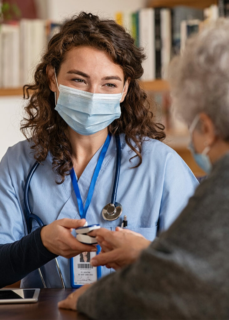 nurse with a mask on talking to an elderly patient