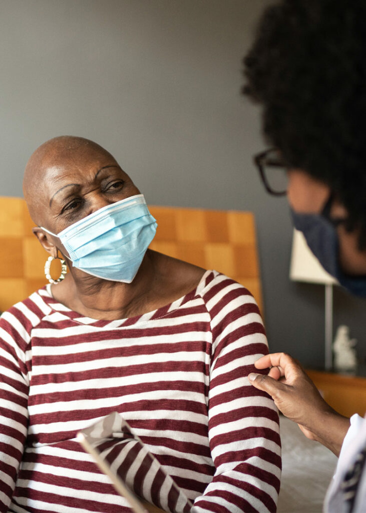 elderly woman with a mask on talking to a nurse in patient care